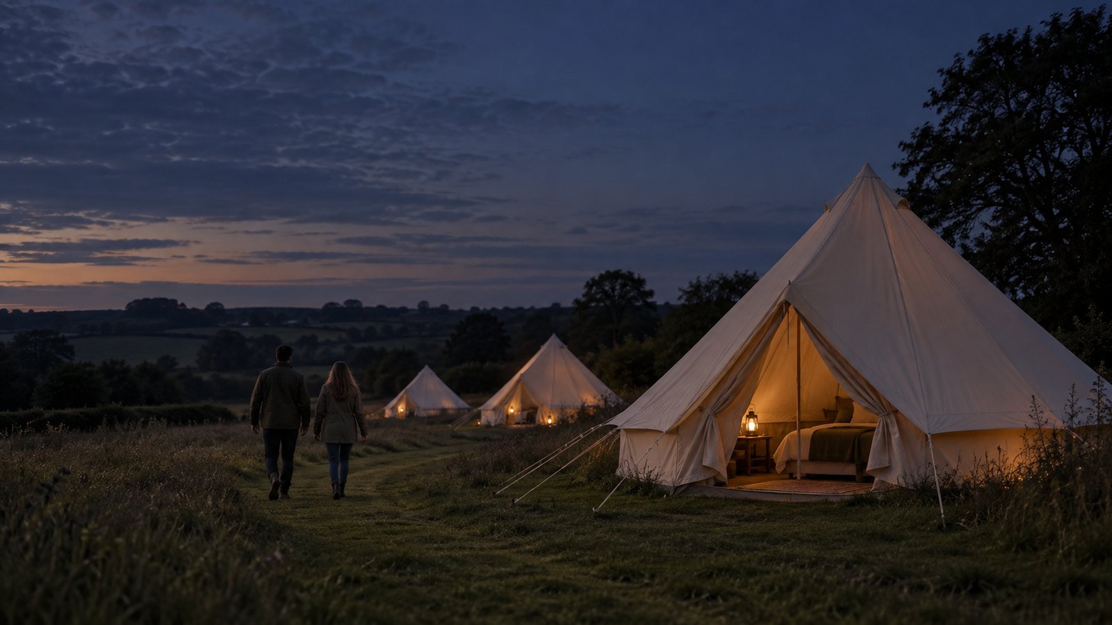 Illustrative evening scene of two guests walking towards warmly lit cream bell tents in an English meadow.